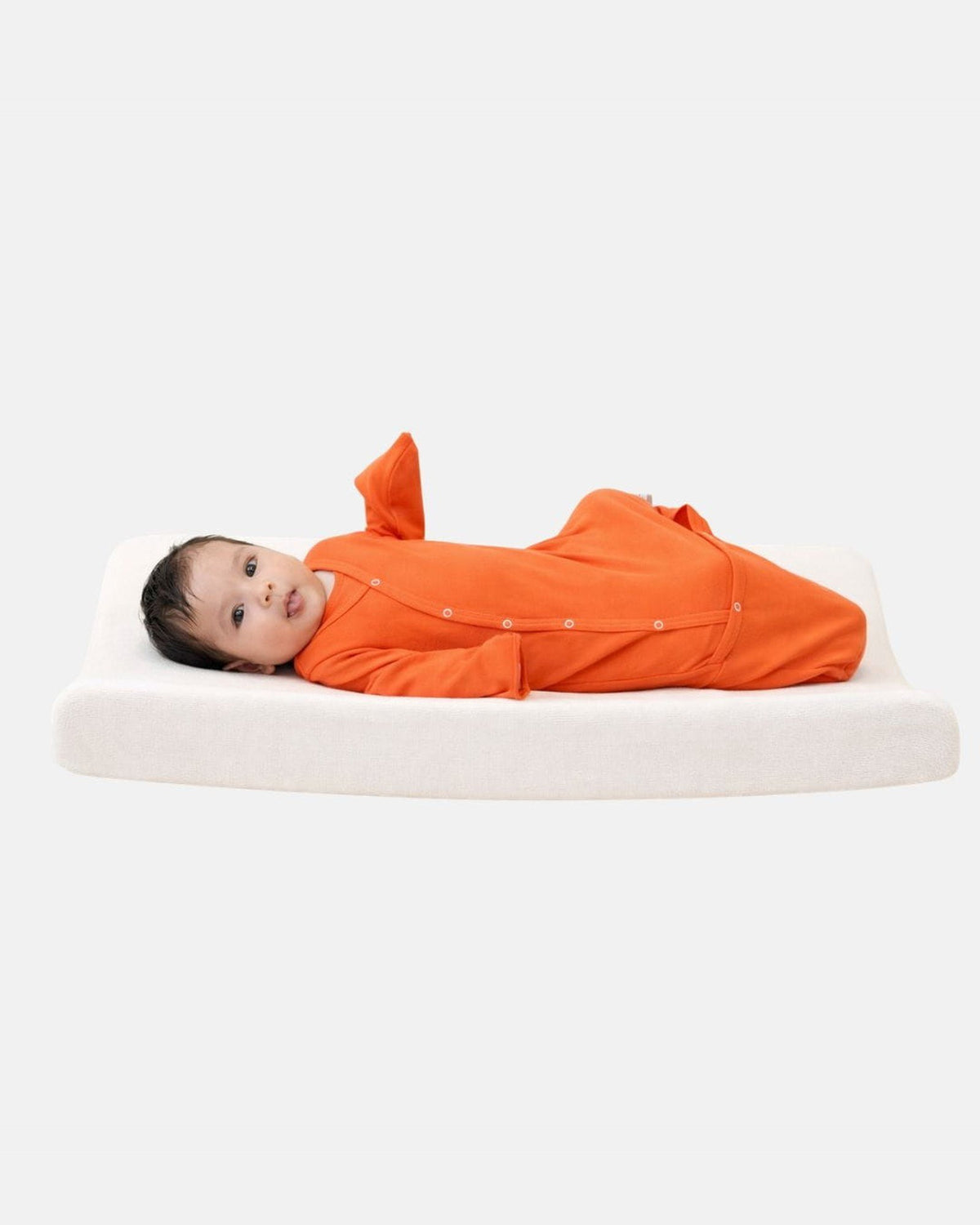 Baby ligt op verschoonkussen in SleepyBeebi cognac, omslagbare voetjes open