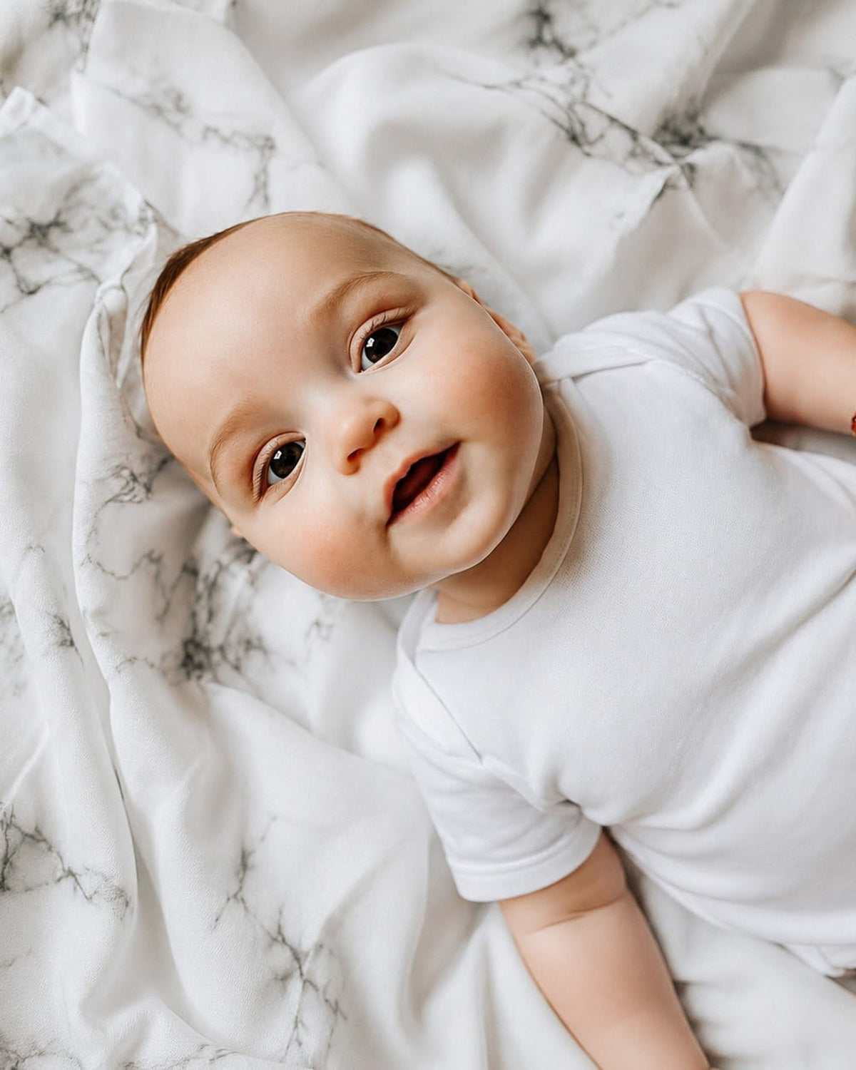 Baby ligt lachend op een MIMMTI hydrofiele doek met marmerprint