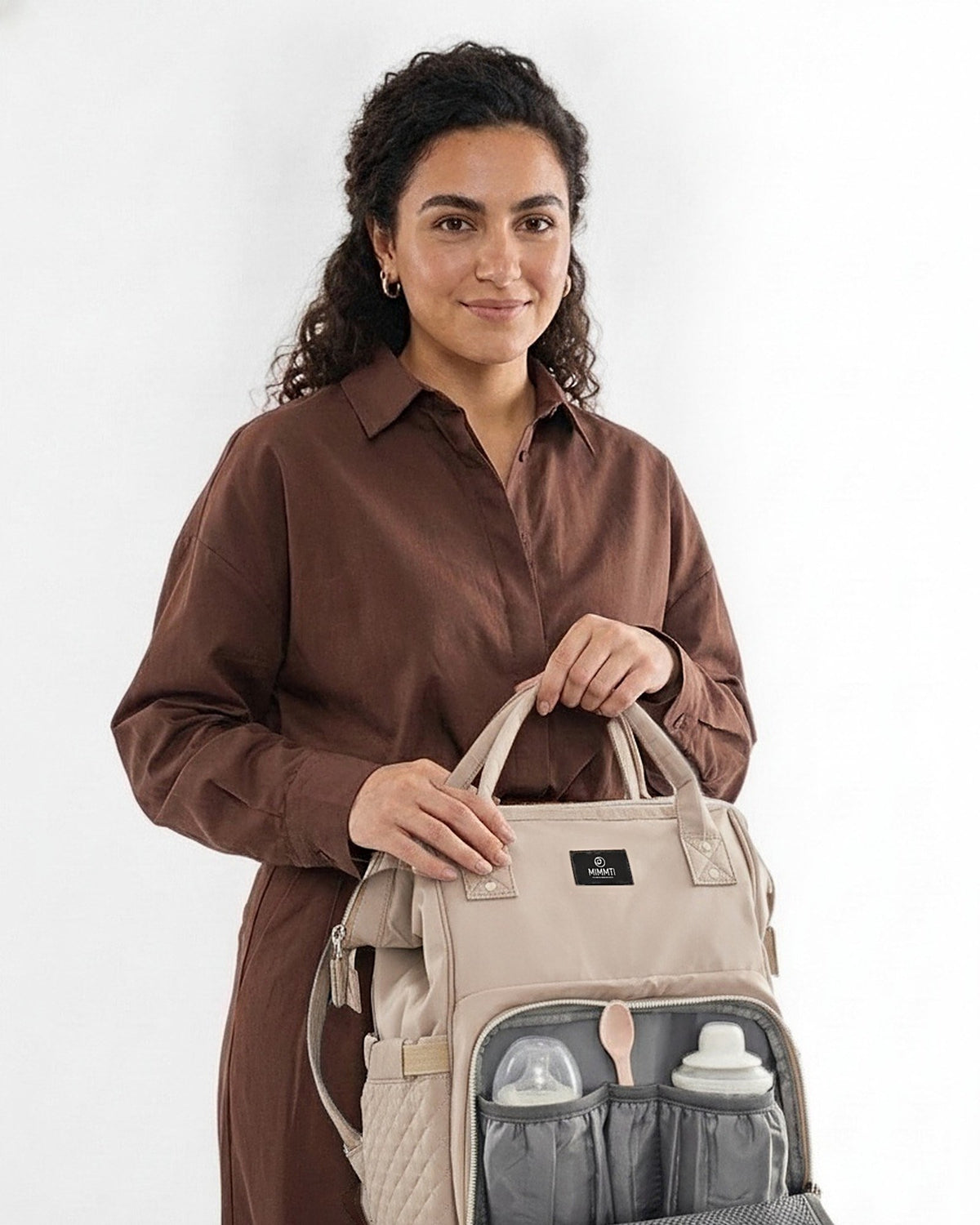 Moeder pakt een flesje uit de MIMMTI 1.0 luiertas rugzak in beige taupe