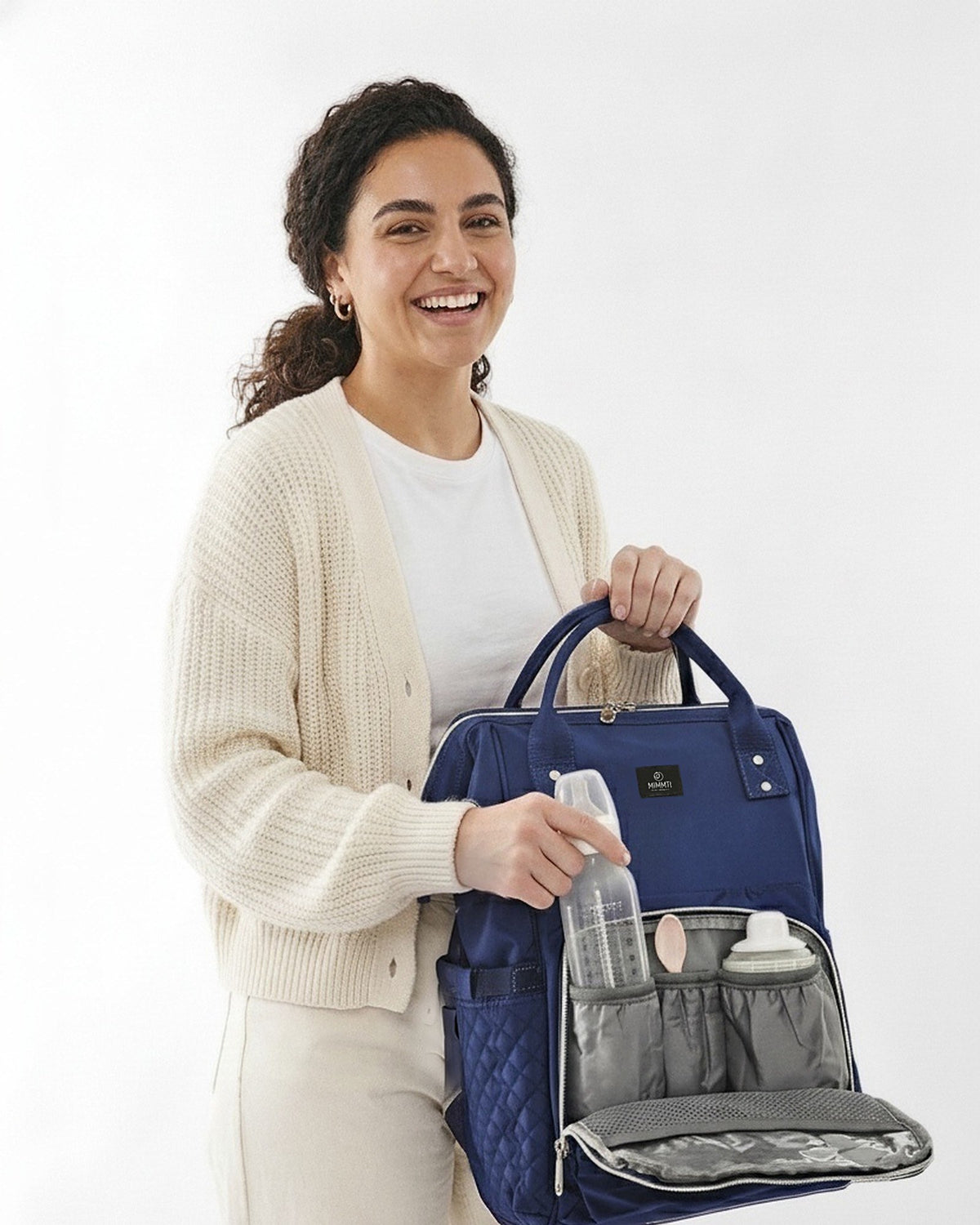 Moeder pakt een flesje uit de MIMMTI 1.0 luiertas rugzak in blauw