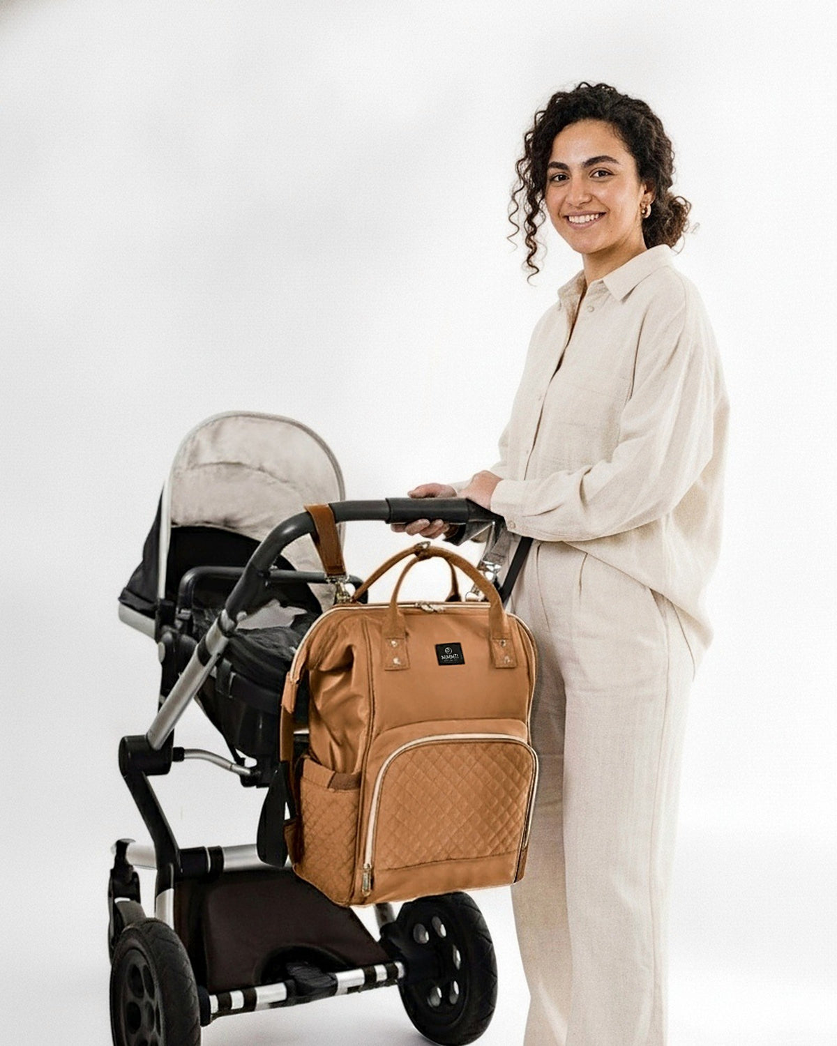 Moeder bij de kinderwagen met de MIMMTI 1.0 luiertas rugzak in cognac