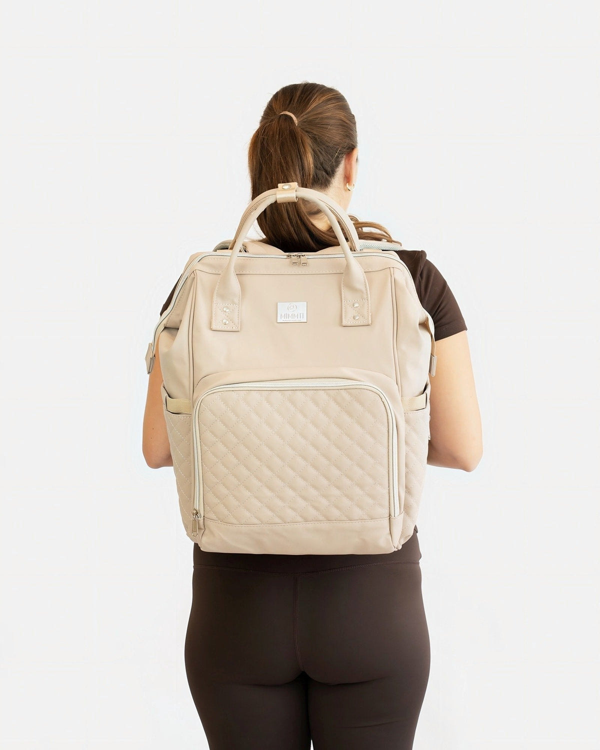 MIMMTI 2.0 luiertas rugzak in beige, gedragen door een moeder