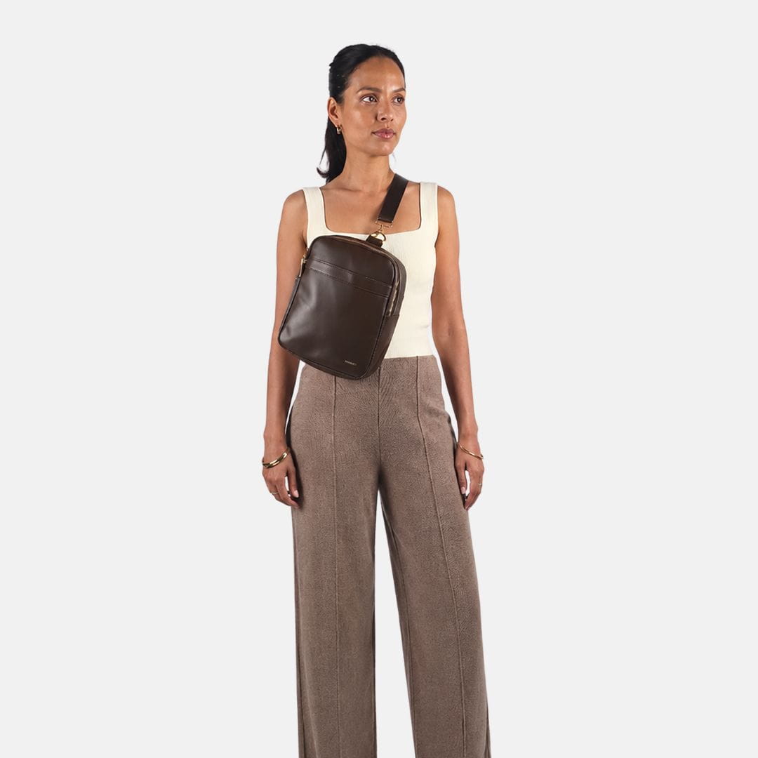 Vrouw draagt de MIMMTI Zoya luiertas in espresso crossbody voor op de borst