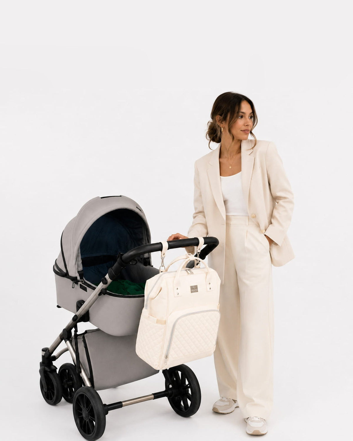 Vrouw met kinderwagen, MIMMTI 2.0 luiertas rugzak in crème aan de duwstang