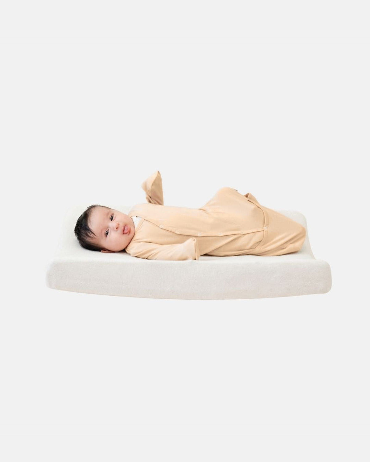 Baby ligt op verschoonkussen in SleepyBeebi beige, omslagbare voetjes open